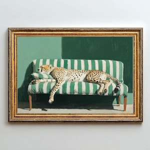 Op de afbeelding: Een ingelijst schilderij toont een cheetah die rust op een groen en wit gestreepte bank. De gevlekte vacht van de cheetah contrasteert met het patroon van de bank. De achtergrond is effen groen, met een schaduw die diepte toevoegt. De lijst is goudkleurig.
