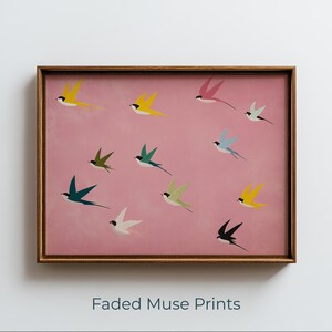May include: A framed print featuring a pink background with colorful stylized birds in flight. The birds are in various colors, including yellow, green, and blue. The frame is a warm brown color. The text "Faded Muse Prints" is at the bottom.