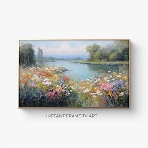 Puede incluir: Una pintura de paisaje enmarcada representa una serena escena de río con coloridas flores silvestres en primer plano. La obra de arte tiene un marco dorado y el texto "INSTANT FRAME TV ART" en la parte inferior.