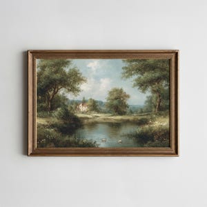 Pode incluir: Pintura de paisagem emoldurada que retrata uma serena cena de lagoa. A obra apresenta uma casa ao longe, rodeada por exuberantes árvores e folhagem verde. O céu é azul suave com nuvens fofas, e a moldura é de cor dourada quente.