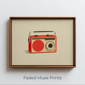 May include: A framed art print featuring a red and beige portable radio illustration centered on a light background. The radio has a black handle, a large circular speaker, a circular tuning dial, and a small red logo in the bottom right corner.