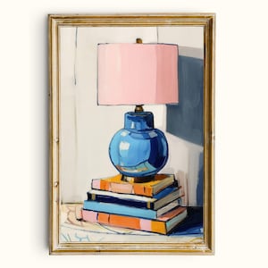 May include: A framed painting depicting a blue lamp with a pink lampshade, set atop a stack of colourful books. The lamp features a spherical base and a gold-coloured detail. The books are in shades of orange, blue, and pink.