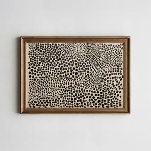 May include: A framed artwork featuring a pattern of black spots on a beige background. The artwork is enclosed in a gold-colored frame, adding a touch of elegance to the piece. The spotted design creates a visually interesting texture.