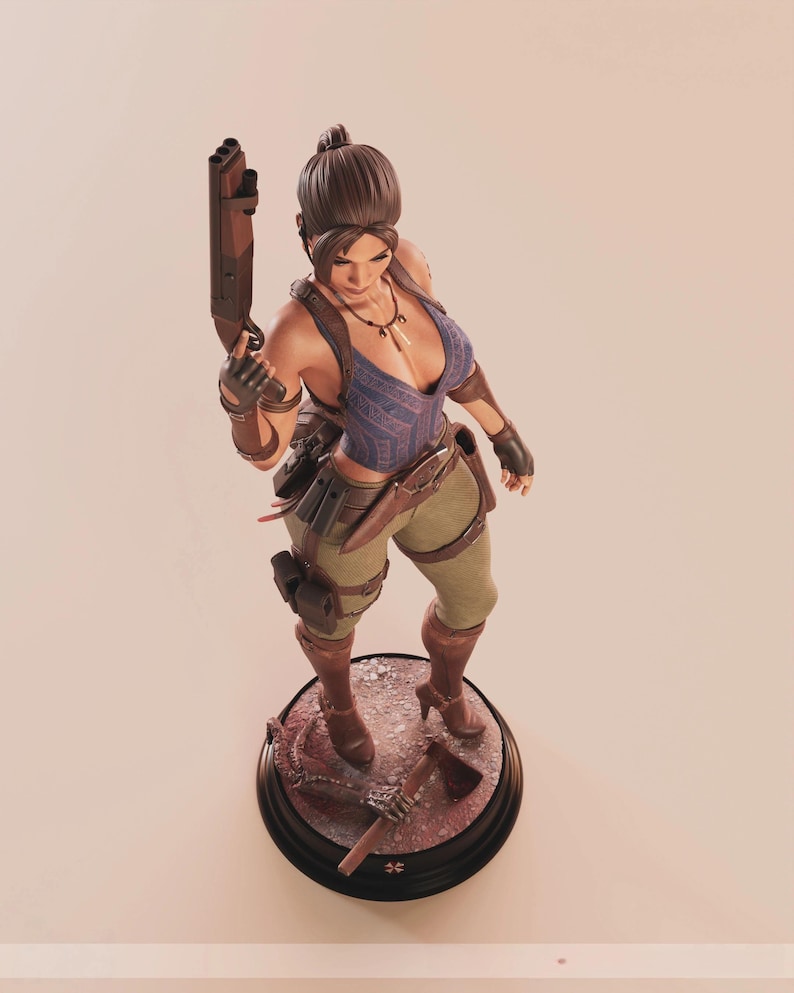 May include: A detailed figurine of a female character in a blue top, khaki pants, and brown boots, holding a rifle. The figure stands on a circular base with a hatchet and other accessories. The character has a ponytail and is wearing gloves.
