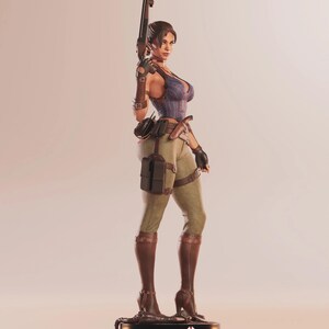 May include: A detailed figurine of a woman in a combat outfit, holding a rifle. She wears a blue and purple corset, olive green pants, and brown boots. The figurine stands on a black base with a red and white emblem.