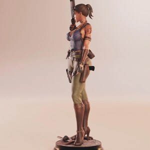 May include: A detailed figurine of a woman in a blue top, green pants, and brown boots, holding a gun. The figure has a ponytail and is standing on a black base. Accessories include a holster and a tattoo on the arm.