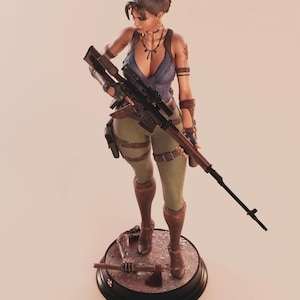 May include: A detailed figurine of a female character holding a rifle, dressed in a blue top, green pants, and brown boots. The figure stands on a circular base with an axe. The figurine has a tattoo on her arm.