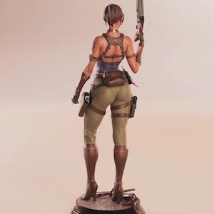 May include: A detailed figurine of a woman in combat attire, viewed from the back. She wears a blue top, olive green pants, and brown boots. She holds a shotgun and has various pouches and holsters. The figure stands on a black base.