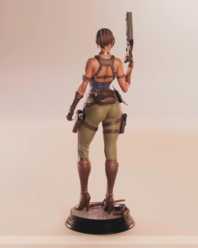 May include: A detailed figurine of a woman in combat attire, viewed from the back. She wears a blue top, olive green pants, and brown boots. She holds a shotgun and has various pouches and holsters. The figure stands on a black base.