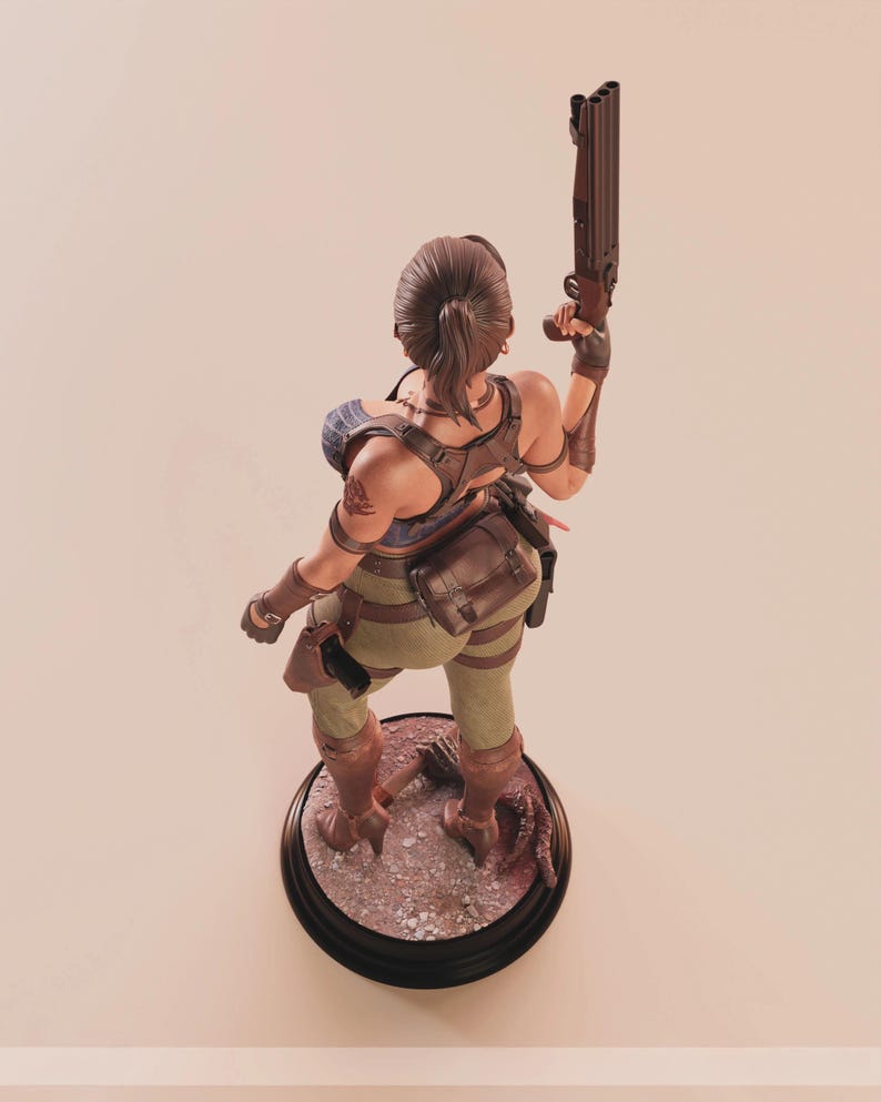May include: A detailed figurine of a female character in combat gear, holding a shotgun. The figure is posed on a circular base with a detailed, textured surface. The character wears a brown leather harness, green pants, and brown boots.