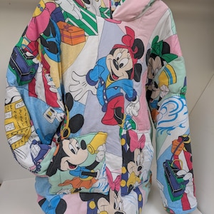 K&ouml;nnte beinhalten: Ein Patchwork-Hoodie mit Disney-Figuren wie Mickey und Minnie Mouse. Der Hoodie besteht aus bunten Stoffbahnen mit Cartoon-Grafiken, einer Kapuze und einer Vordertasche. Die &Auml;rmel sind lang und der Stil ist &uuml;bergro&szlig;.