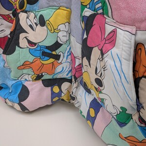 K&ouml;nnte beinhalten: Nahaufnahme eines Patchwork-Stoffs mit Micky und Minnie Maus. Der Stoff ist eine Mischung aus farbenfrohen Mustern und Drucken mit Bildern der ikonischen Zeichentrickfiguren. Die Taschen sind aus dem gleichen Stoff gefertigt.