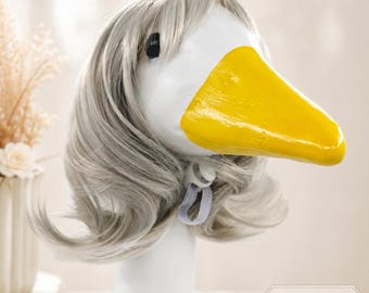 May include: A white goose head figurine featuring a bright yellow beak and a shoulder-length, layered light gray wig with bangs. The wig is secured with a white elastic strap under the chin. A small rectangular label in the corner reads Style A.