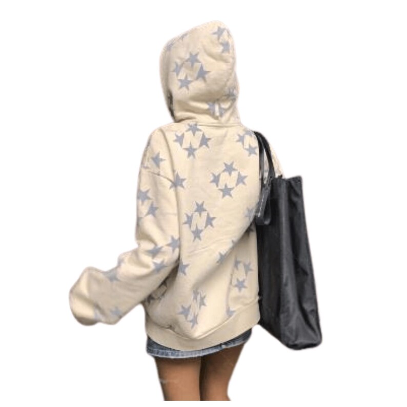 Puede incluir: Sudadera con capucha color crema con un patr&oacute;n repetido de estrellas azul claro. La sudadera tiene capucha y mangas largas. Un bolso tote negro cuelga del hombro. La persona lleva una falda vaquera.