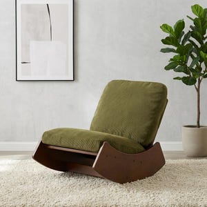 Pu&ograve; includere: Una moderna sedia a dondolo con struttura in legno marrone scuro e cuscini in velluto a coste verde oliva. La sedia &egrave; appoggiata su un tappeto shaggy bianco, con un'opera d'arte astratta incorniciata sulla parete.
