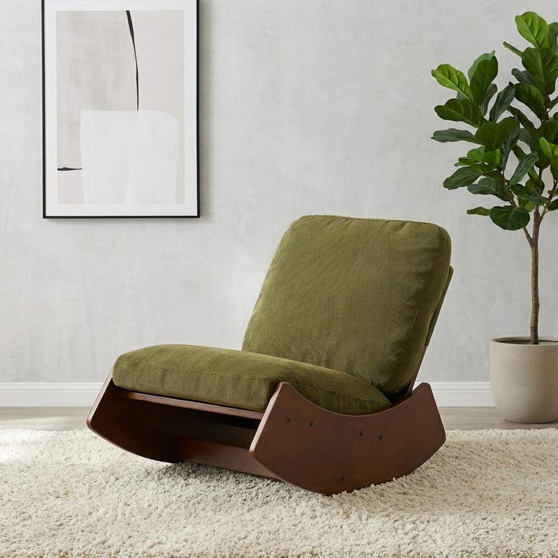 Pu&ograve; includere: Una moderna sedia a dondolo con struttura in legno marrone scuro e cuscini in velluto a coste verde oliva. La sedia &egrave; appoggiata su un tappeto shaggy bianco, con un'opera d'arte astratta incorniciata sulla parete.
