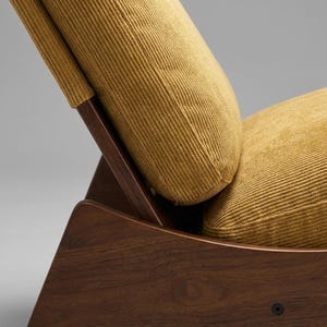 Pu&ograve; includere: Primo piano di una sedia moderna di met&agrave; secolo. La sedia presenta una struttura in legno scuro e cuscini in velluto a coste giallo senape. Il design include supporti angolati e uno schienale curvo.
