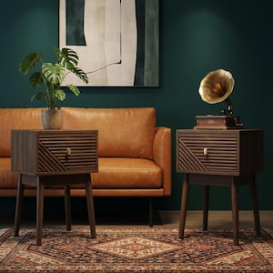 May include: Two dark brown wooden bedside tables with angled legs and a drawer with a geometric design. One table has a potted plant on top, the other has a vintage gramophone. The tables are on a patterned rug.
