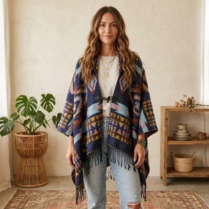 Könnte beinhalten: Ein marineblauer Poncho mit einem geometrischen Muster in Orange-, Gelb- und Türkistönen. Der Poncho hat einen Fransenbesatz und einen schwarzen Verschluss. Die Person trägt ein weißes Hemd und blaue Jeans.