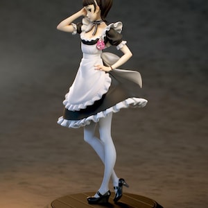 May include: A figurine of a maid in a black and white dress with a ruffled apron and sleeves. The maid is wearing a white headband and holding her hand to her head. She is standing on a round, dark brown base.