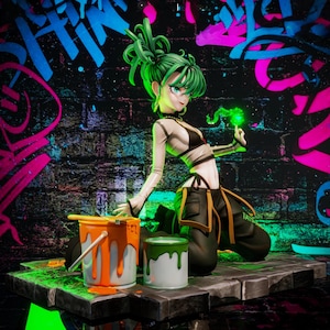 May include: A figurine of a female character with green hair and eyes, dressed in a white and black outfit, kneels near paint cans. The background features graffiti art in blue, pink, and green on a brick wall.