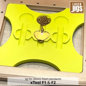 May include: A bright yellow laser jig for 20mm heart pendants, compatible with xTool F1 and F2, featuring a central cutout holding a gold-colored heart pendant on a matching chain, with additional empty slots for positioning multiple items.