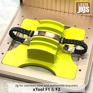 May include: A black braided leatherette bracelet with a polished stainless steel centre plate and clasp, secured in a bright yellow laser engraving jig. The jig features the text Laser Jigs and the label Jig for stainless steel and leatherette bracelets xTool F1 & F2.