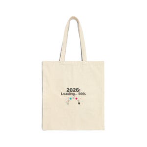 May include: A cream-coloured tote bag with long handles. The bag has the text "2026: Loading... 99%" in black, with a colourful loading bar graphic below. The bag is made of a sturdy fabric.