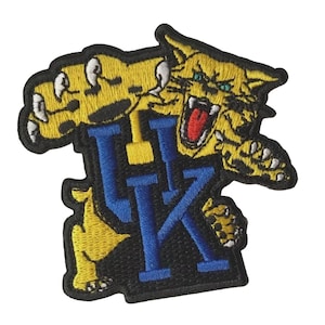 May include: Embroidered patch featuring a yellow wildcat with blue and yellow accents, claws extended, and mouth open. The patch includes the letters "UK" in blue, with a black border. Ideal for jackets, bags, or other fabric items.