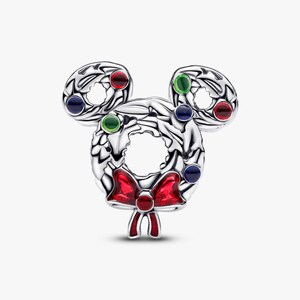 A silver-colored charm in the shape of a wreath, adorned with colorful gemstones and a red bow.