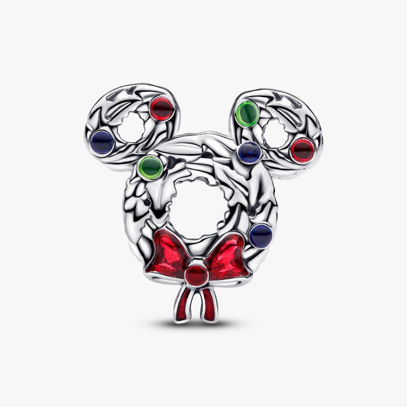 A silver-colored charm in the shape of a wreath, adorned with colorful gemstones and a red bow.