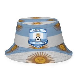 May include: A white and light blue bucket hat featuring the Argentinian flag design. The hat has a repeating pattern of suns and a central emblem with the text "ARGENTINA" and "PASIÓN ALBICELSTE" with a soccer ball.