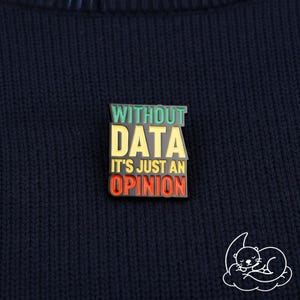Könnte beinhalten: Rechteckiger Emaille-Pin mit dem Text "WITHOUT DATA IT'S JUST AN OPINION" in Grün, Gelb und Rot. Der Pin ist auf einem dunkelblauen Strickstoff angebracht. Eine weiße Illustration eines schlafenden Otters befindet sich in der unteren rechten Ecke.