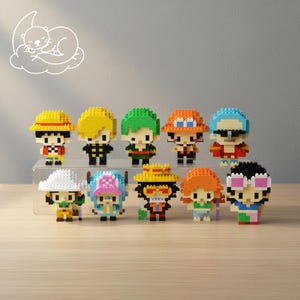 May include: A collection of ten pixelated character figurines, each with distinct outfits and hairstyles. The figures are arranged on a clear display stand. The characters are in various colors, including yellow, green, orange, and blue.