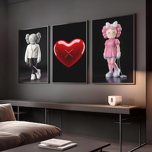 Peut inclure: Trois œuvres d'art encadrées représentant des personnages de pop art et un cœur sur fond noir. L'art comprend une figurine en veste blanche, un cœur rouge avec un X et une figurine en robe rose. L'art est exposé au-dessus d'une console grise foncée.