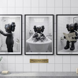 May include: A set of three framed prints titled KAWS: THE BATHROOM CHRONICLES. Each print features a black KAWS character in a white tiled bathroom setting: one in the shower, one in a bathtub, and one sitting on a toilet reading a newspaper.