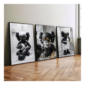 May include: A set of three framed wall art prints featuring a black cartoon character with X-shaped eyes in a bathroom setting. The first print shows the character bathing, the second shaving, and the third standing with a white towel.
