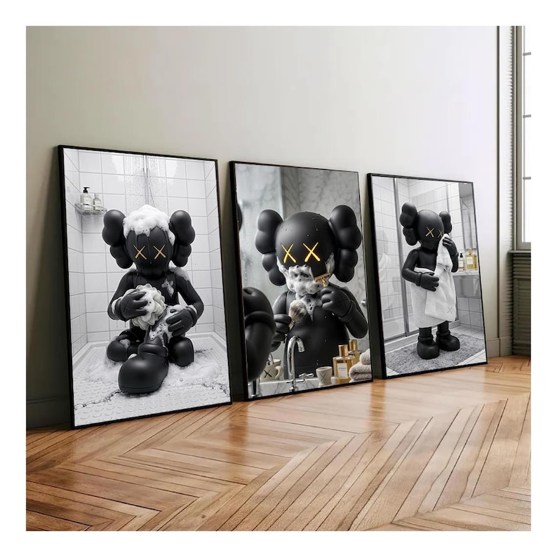 May include: A set of three framed wall art prints featuring a black cartoon character with X-shaped eyes in a bathroom setting. The first print shows the character bathing, the second shaving, and the third standing with a white towel.
