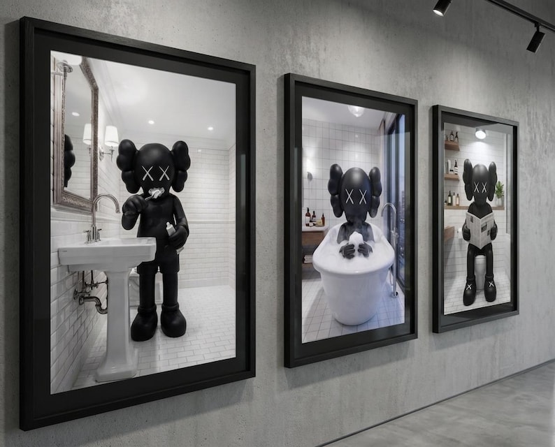 May include: Three framed art pieces featuring a black figure in a bathroom setting. The figure is depicted brushing its teeth, bathing in a tub, and reading a newspaper. The frames are black and mounted on a gray wall.
