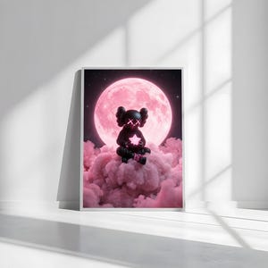 May include: Framed art print showing a black figure with 'X' eyes holding a glowing star, sitting on pink clouds. A large pink moon and starry night sky are in the background. The artwork is presented in a white frame.