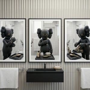 May include: A triptych of framed wall art prints featuring a matte black KAWS character in a bathroom setting. The left print shows the figure adjusting a watch, the centre shows it brushing teeth, and the right shows it holding a gold and black sneaker.