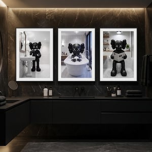 May include: Three framed black and white prints featuring a cartoon character in a bathroom setting. The character is depicted in various bathroom activities, including washing hands, bathing, and reading a newspaper. The prints are displayed above a black vanity in a modern bathroom.