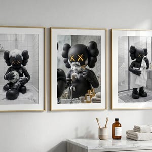 May include: A set of three framed wall art prints featuring a black KAWS-style character in a bathroom setting. The first print shows the character bathing, the second shows it shaving, and the third shows it drying off with a white towel.