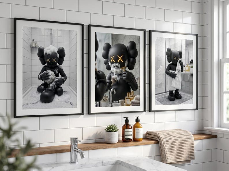 May include: A set of three framed wall art prints featuring a black KAWS character in a bathroom setting. The first shows the figure bathing, the second shaving in a mirror, and the third drying off with a white towel. Each print has a black frame.