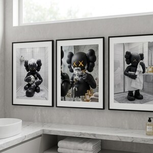 May include: A set of three framed wall art prints featuring a black cartoon character with X-shaped eyes in a bathroom setting. The first print shows the character bathing, the second shaving, and the third drying off with a white towel.