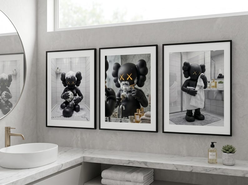 May include: A set of three framed wall art prints featuring a black cartoon character with X-shaped eyes in a bathroom setting. The first print shows the character bathing, the second shaving, and the third drying off with a white towel.