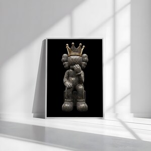 Pu&ograve; includere: Opera d'arte incorniciata con una figura seduta con una corona d'oro. La figura &egrave; grigio scuro con venature dorate, seduta su un blocco grigio scuro su sfondo nero. L'opera &egrave; esposta in una cornice bianca.