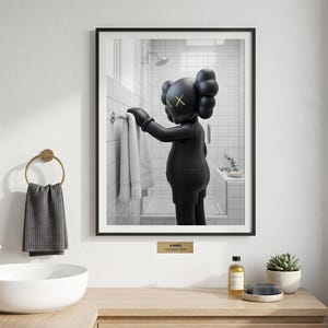 May include: A framed wall art print featuring a black KAWS Companion figure standing in a white tiled bathroom, reaching for a white towel on a rack. The figure has signature X-shaped eyes. A small gold plaque below the frame reads KAWS Companion Bath.