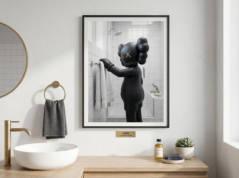 May include: A framed wall art print featuring a black KAWS Companion figure standing in a white tiled bathroom, reaching for a white towel on a rack. The figure has signature X-shaped eyes. A small gold plaque below the frame reads KAWS Companion Bath.