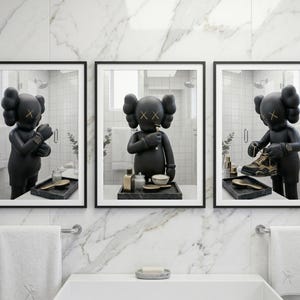 May include: A set of three framed wall art prints featuring a black KAWS character in a bathroom setting. The character is shown adjusting a watch, brushing teeth, and holding a sneaker. Each print is displayed in a thin black frame.